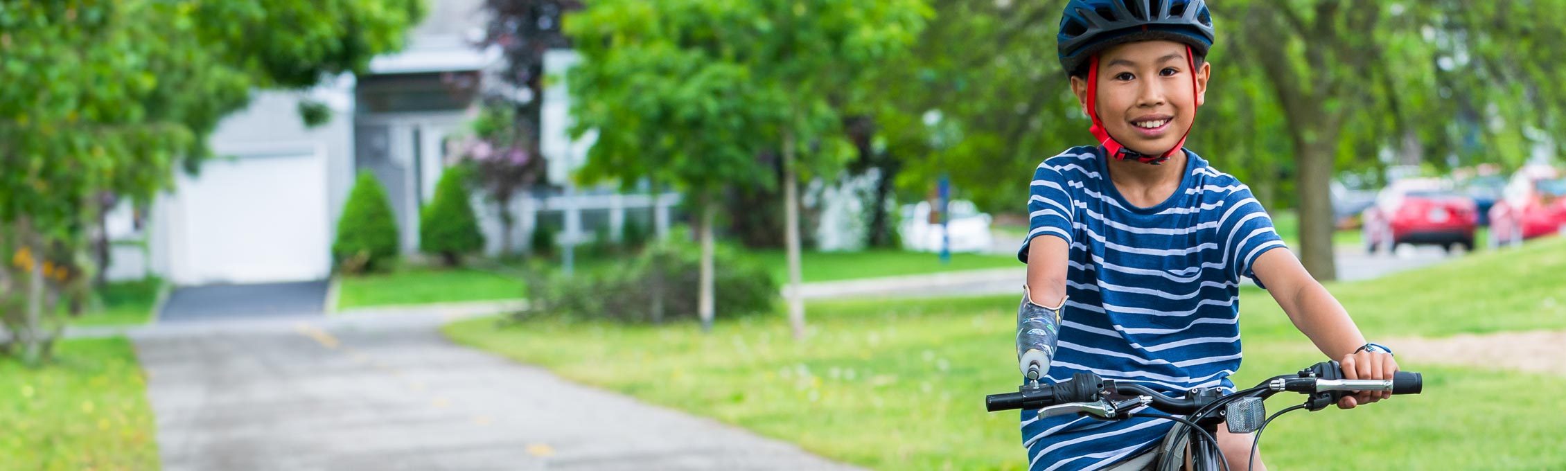 Un jeune garçon amputé d'un bras fait du vélo dans un parc à l'aide d'un appareil fixé à son guidon.